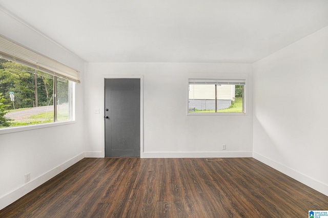 spare room featuring dark wood-type flooring, visible vents, and baseboards