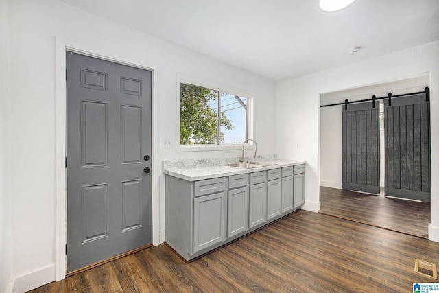 kitchen featuring dark wood-style flooring, gray cabinets, a barn door, a sink, and baseboards