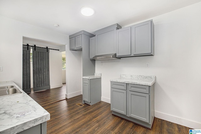 kitchen featuring a barn door, baseboards, dark wood-type flooring, gray cabinets, and light countertops