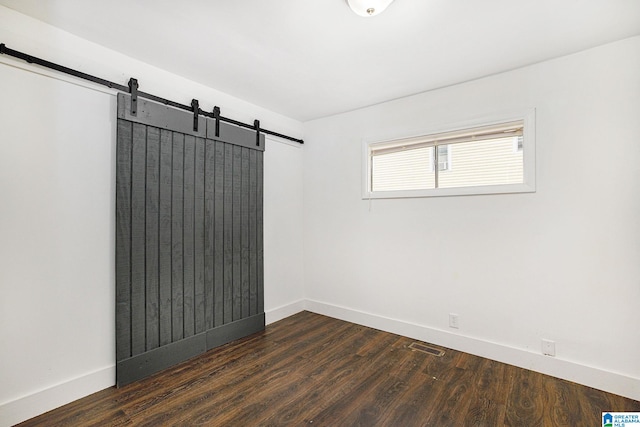 unfurnished room featuring a barn door, visible vents, baseboards, and dark wood-style flooring