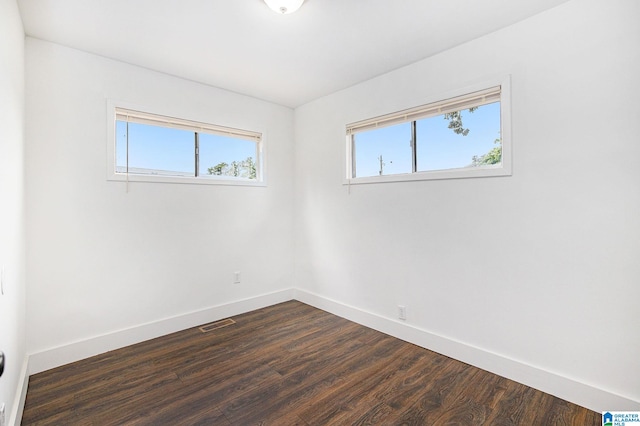 spare room featuring dark wood-style flooring, visible vents, and baseboards