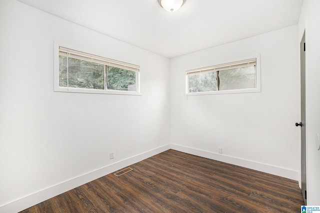 unfurnished room with dark wood-style flooring, visible vents, and baseboards