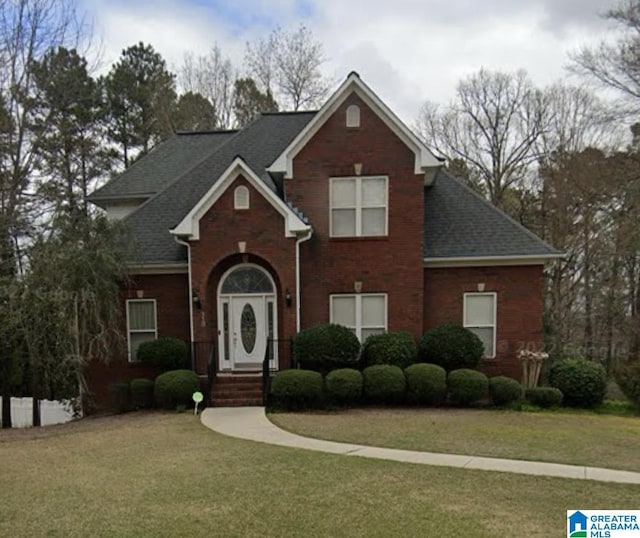 traditional home with a shingled roof, a front yard, and brick siding