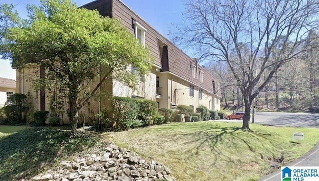 view of side of property featuring a yard, mansard roof, and brick siding