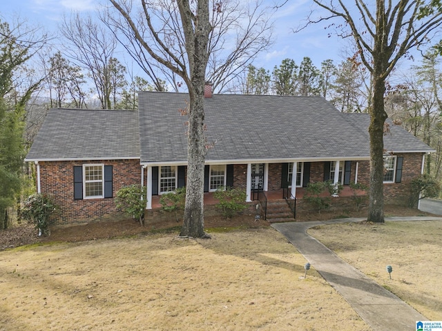 view of front of house with covered porch, brick siding, a chimney, and a shingled roof