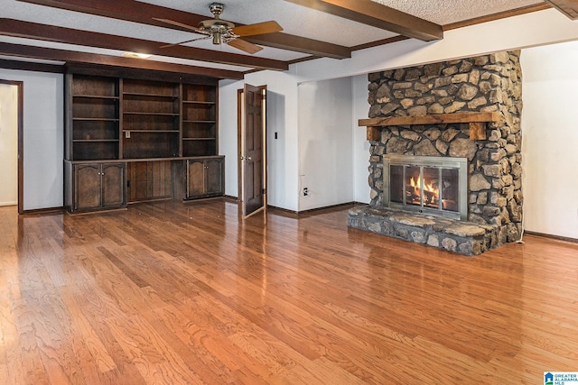 unfurnished living room with a textured ceiling, a stone fireplace, wood finished floors, a ceiling fan, and baseboards