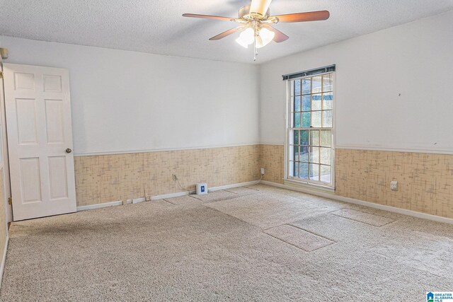 unfurnished room featuring a wainscoted wall, a textured ceiling, a ceiling fan, and carpet flooring