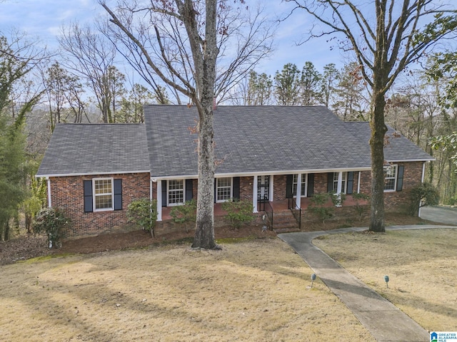 view of front of home with brick siding, a front lawn, a porch, and a shingled roof