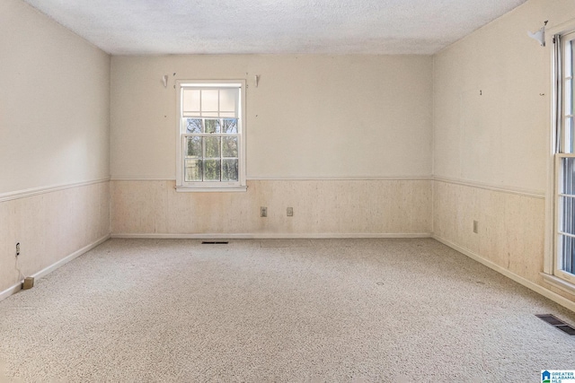 unfurnished room featuring visible vents, carpet flooring, wainscoting, wooden walls, and a textured ceiling