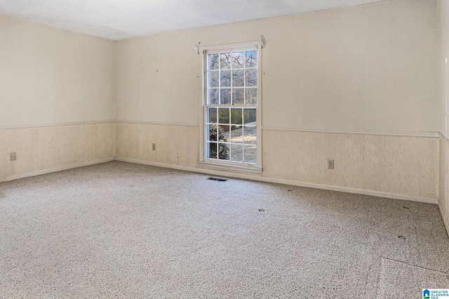 carpeted spare room with wood walls, visible vents, and wainscoting