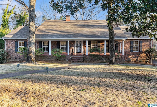 view of front of property with a front yard, a chimney, a porch, and brick siding