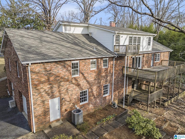 exterior space with a garage, central AC unit, a chimney, a wooden deck, and brick siding