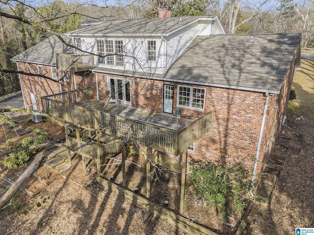 rear view of house featuring brick siding, a chimney, a balcony, and roof with shingles