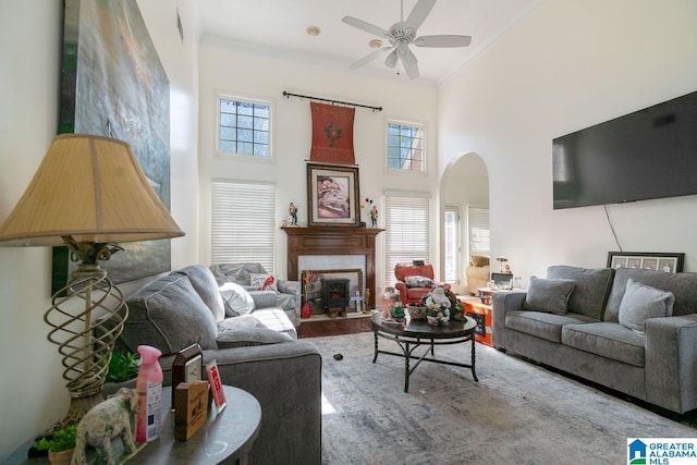 living room with arched walkways, ceiling fan, a fireplace, a towering ceiling, and ornamental molding