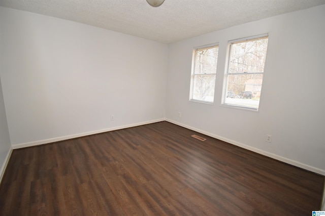 empty room featuring visible vents, a textured ceiling, baseboards, and dark wood-style flooring