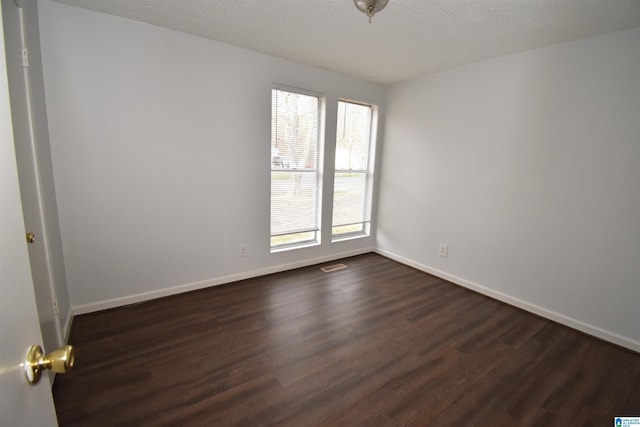 spare room with dark wood-style floors, baseboards, visible vents, and a textured ceiling