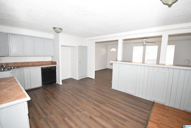 kitchen featuring a textured ceiling, a sink, black dishwasher, light countertops, and dark wood finished floors