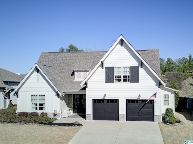 view of front of home with driveway, a shingled roof, stone siding, an attached garage, and board and batten siding