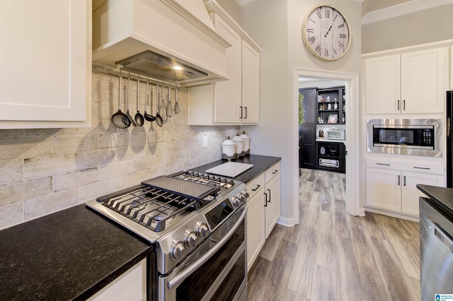 kitchen featuring light wood-type flooring, white cabinetry, custom range hood, and appliances with stainless steel finishes