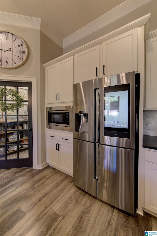 kitchen with stainless steel appliances, light wood-style floors, white cabinetry, and crown molding