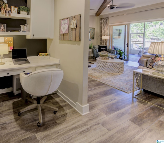 office area featuring built in desk, beamed ceiling, wood finished floors, and baseboards