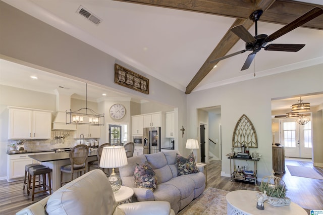 living area featuring a wealth of natural light, beam ceiling, visible vents, and stairs