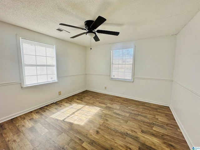 unfurnished room with a textured ceiling, wood finished floors, visible vents, and a healthy amount of sunlight