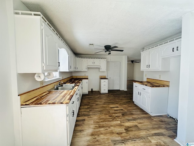 kitchen with dark wood finished floors, white cabinets, a sink, a textured ceiling, and wood counters