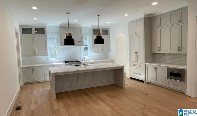 kitchen with a kitchen island with sink, visible vents, light countertops, light wood finished floors, and crown molding