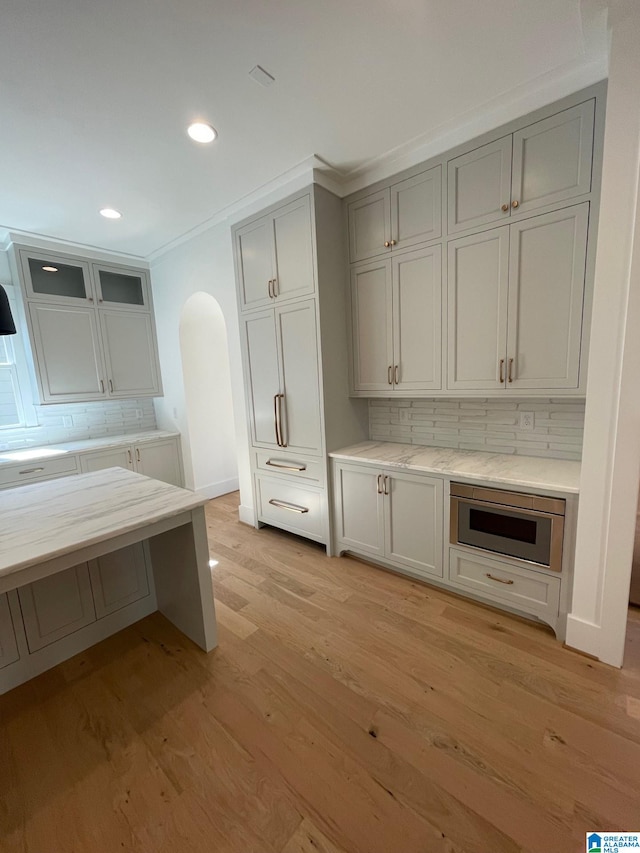 kitchen with arched walkways, stainless steel microwave, backsplash, gray cabinetry, and light wood-style floors