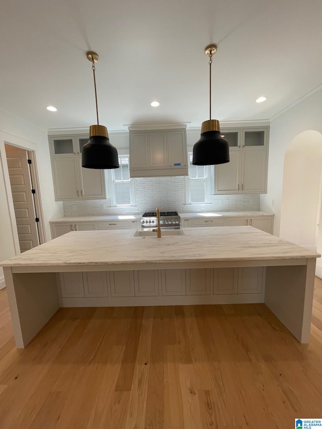 kitchen with light wood-type flooring, tasteful backsplash, arched walkways, and glass insert cabinets