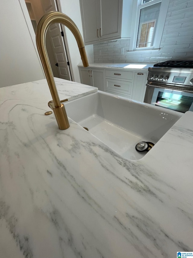 details featuring light stone counters, stainless steel gas stove, a sink, and decorative backsplash