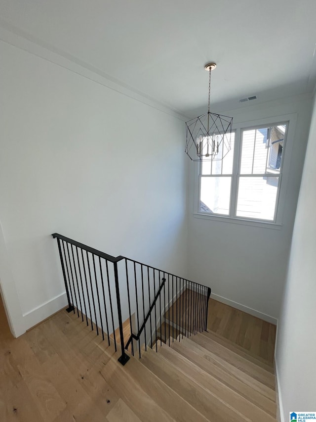 stairs with an inviting chandelier, wood finished floors, visible vents, and baseboards