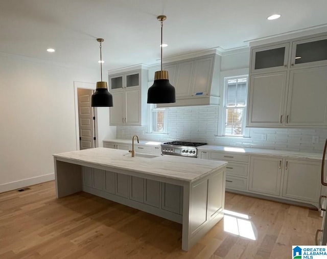 kitchen featuring light wood-style flooring, stove, a sink, backsplash, and glass insert cabinets