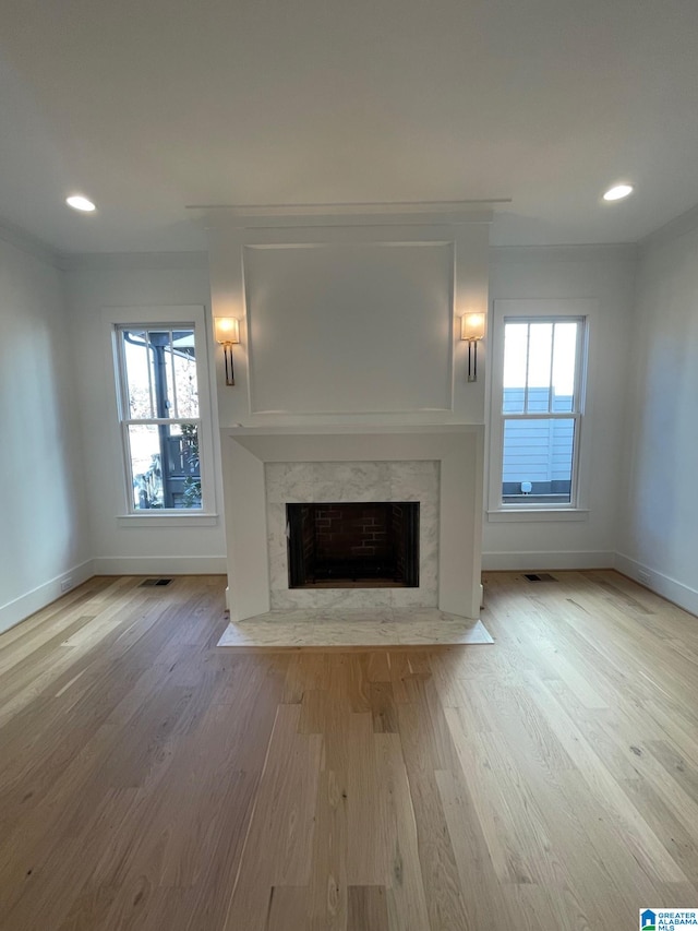 unfurnished living room with a high end fireplace, visible vents, plenty of natural light, and wood finished floors