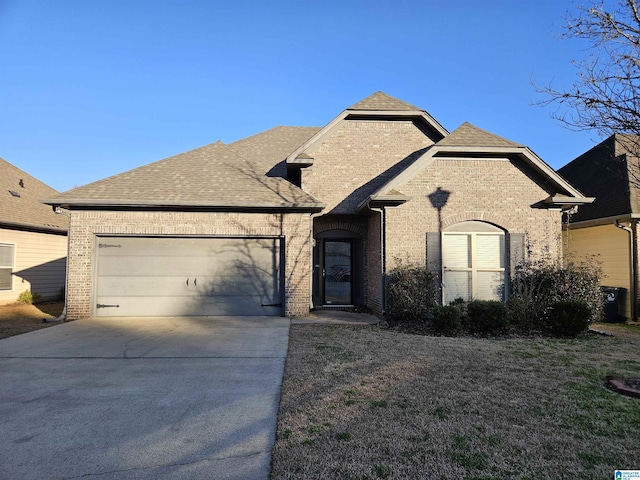 french country style house with driveway, an attached garage, roof with shingles, and brick siding