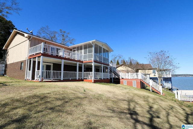 back of property featuring a lawn, a sunroom, a water view, stairs, and brick siding