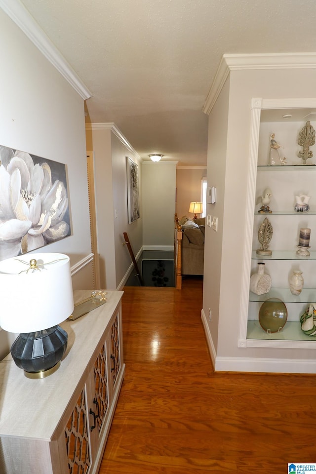 corridor with built in shelves, ornamental molding, an upstairs landing, wood finished floors, and baseboards