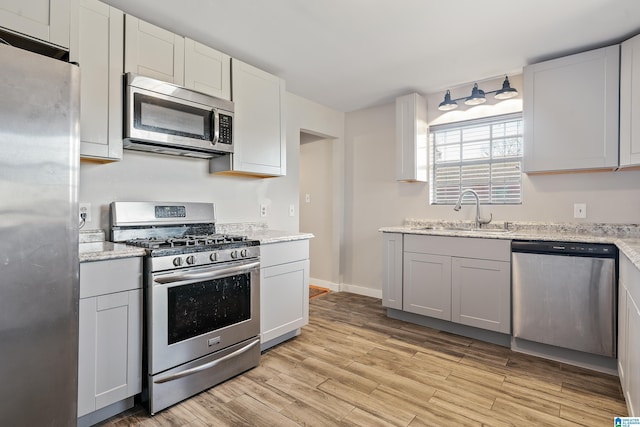 kitchen with light stone counters, stainless steel appliances, light wood-type flooring, and a sink