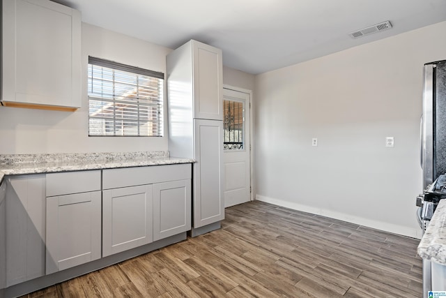 kitchen featuring light stone counters, visible vents, baseboards, and light wood finished floors