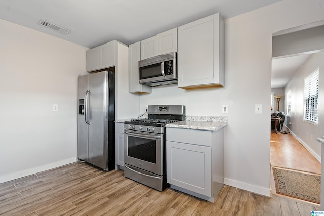 kitchen featuring light wood-style flooring, light stone countertops, visible vents, and stainless steel appliances