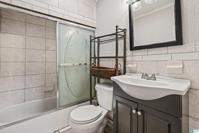 bathroom with vanity, bath / shower combo with glass door, tile walls, toilet, and a textured wall