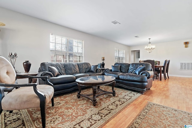 living area featuring a notable chandelier, wood finished floors, visible vents, and baseboards