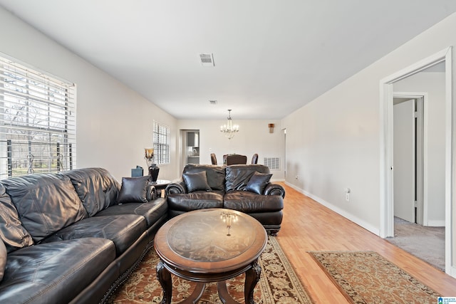 living area featuring visible vents, wood finished floors, baseboards, and a chandelier