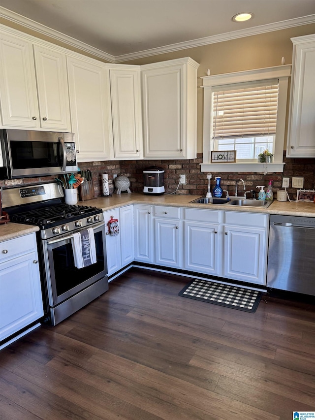 kitchen featuring a sink, white cabinets, appliances with stainless steel finishes, ornamental molding, and dark wood-style floors