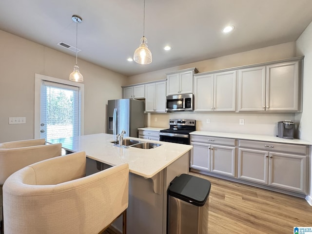 kitchen featuring decorative light fixtures, stainless steel appliances, visible vents, a sink, and light wood-type flooring