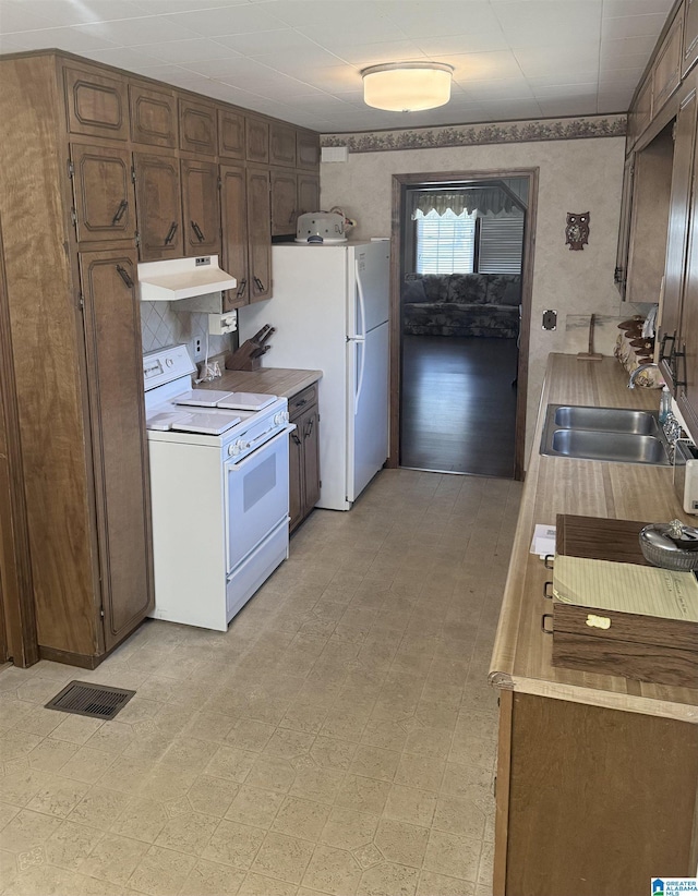 kitchen featuring under cabinet range hood, white appliances, a sink, visible vents, and light floors