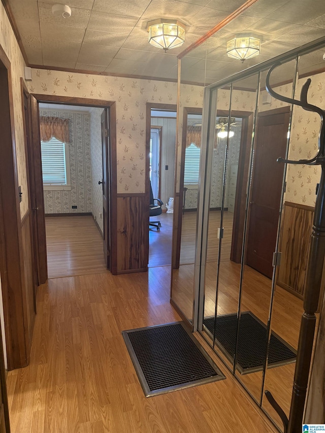 corridor with a wainscoted wall, wood finished floors, and wallpapered walls