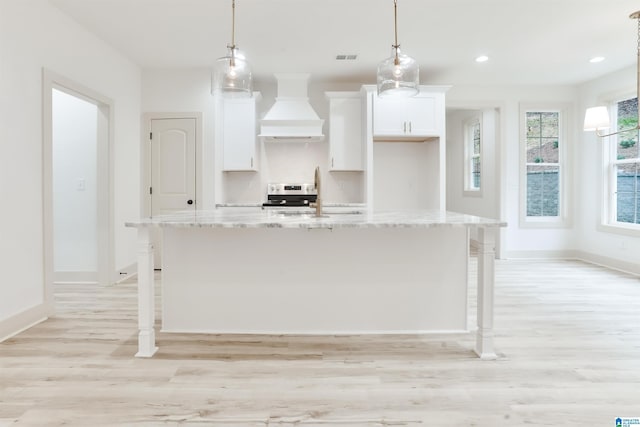 kitchen with white cabinets, an island with sink, custom range hood, a kitchen breakfast bar, and a sink