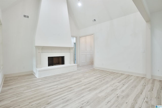 unfurnished living room featuring visible vents, a fireplace with raised hearth, wood finished floors, high vaulted ceiling, and baseboards